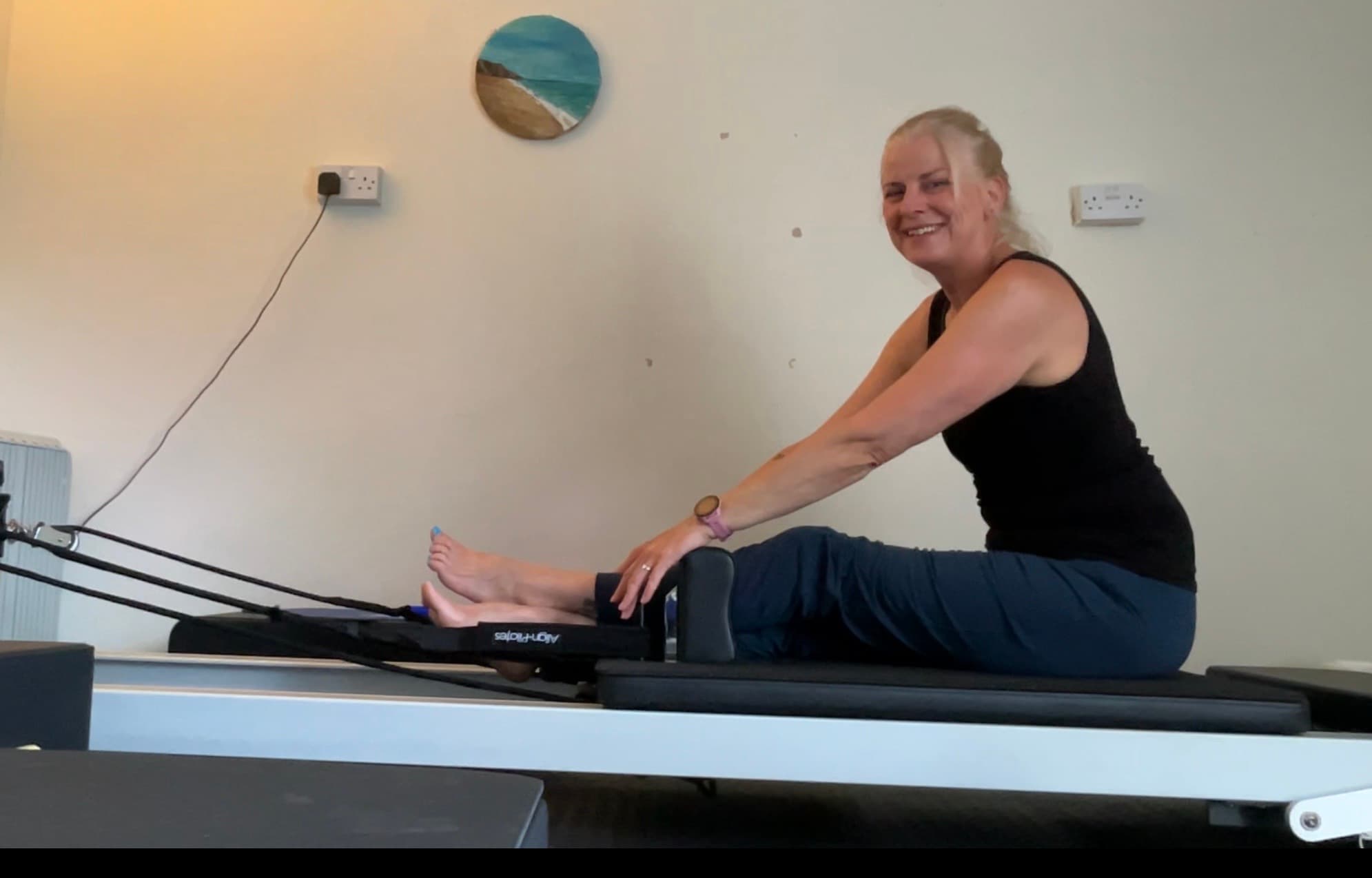 Suzannah, Cornish Core Pilates teacher, smiling on a reformer in the studio at Coombe